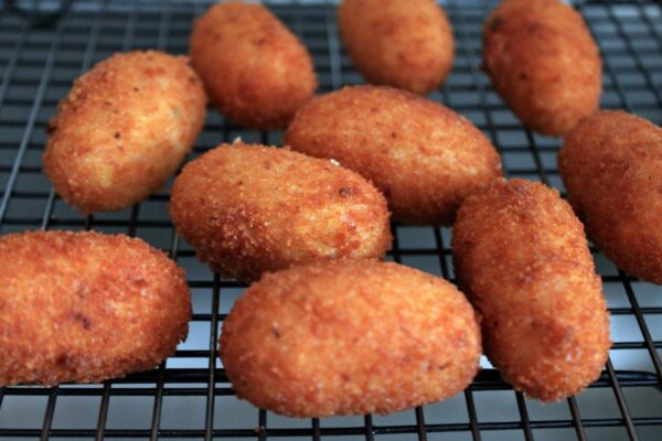 Golden-brown baby shark fish croquette, crispy on the outside and tender inside, served with a zesty lemon wedge and fresh greens